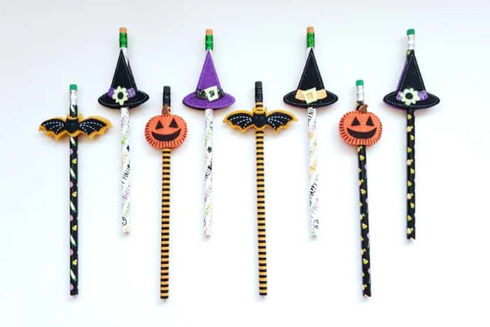 Eight Halloween pencils lined up on table top, bats, hats, and pumpkins.