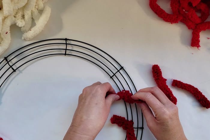 Tying a red piece of yarn around a wreath form wire.