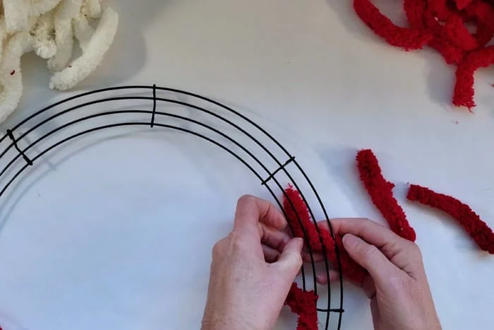 Tying red yarn around the wire of a wreath form.