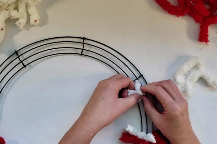 Tying a white piece of fluffy yarn around a wreath form wire.