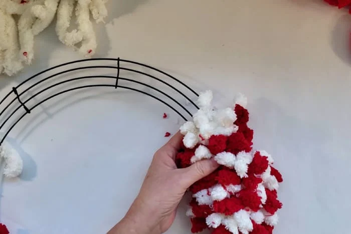 Hand holding wreath form with red and white rows of fluffy yarn.