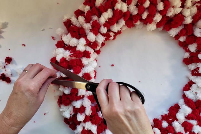 Trimming long ends of yarn from wreath with scissors.