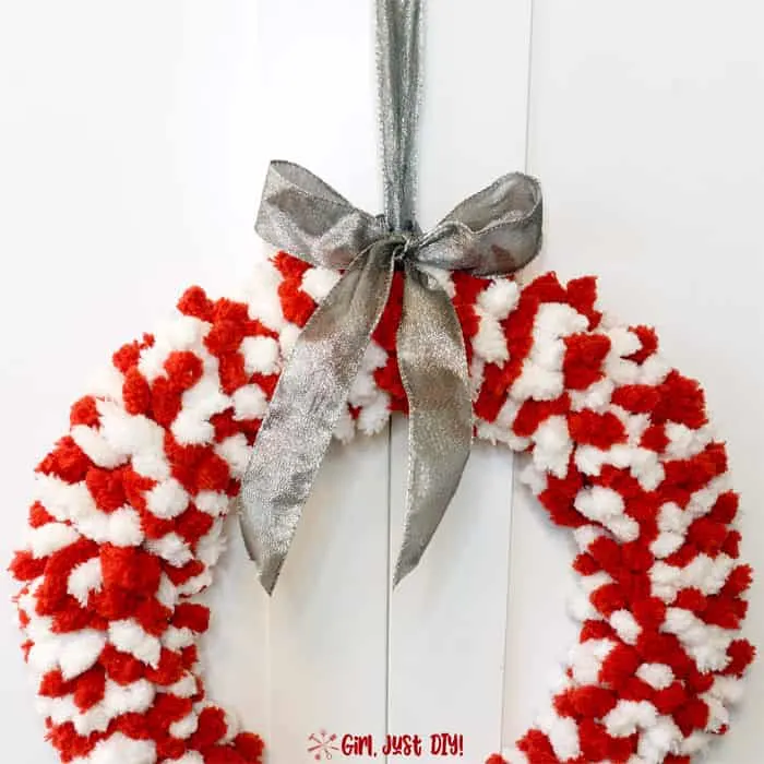 Red and white fluffy christmas wreath with silver ribbon on top.