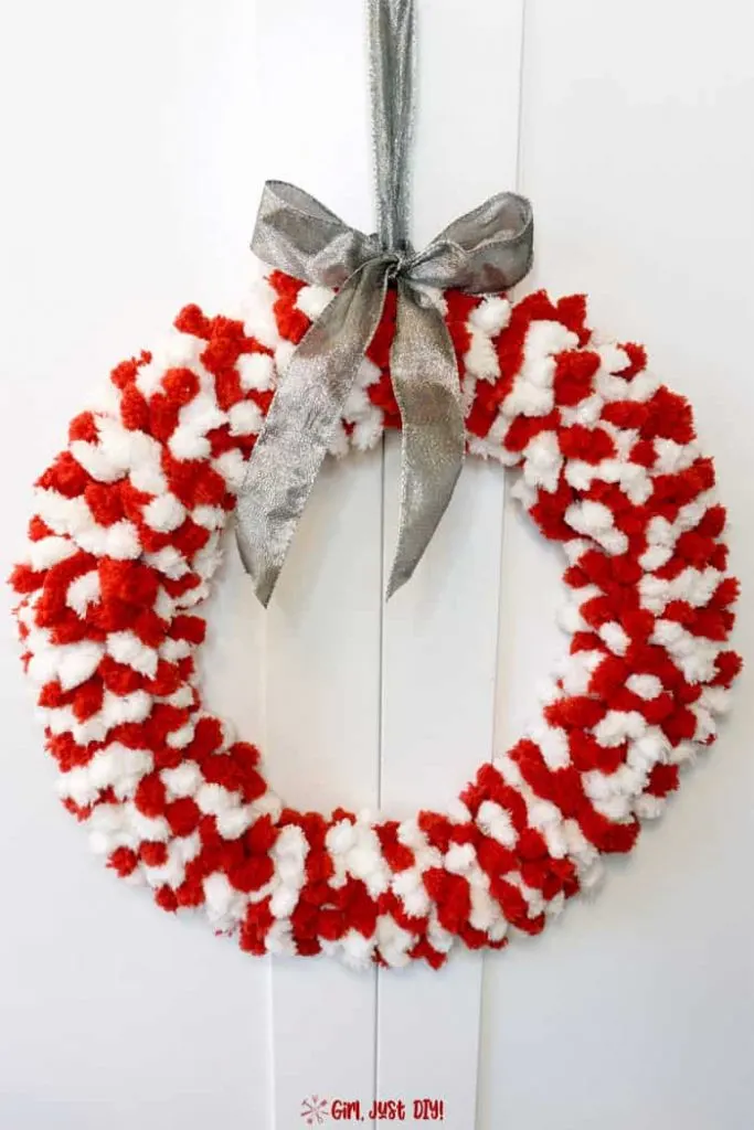 Red and white fluffy christmas wreath with silver bow hanging against a white door.