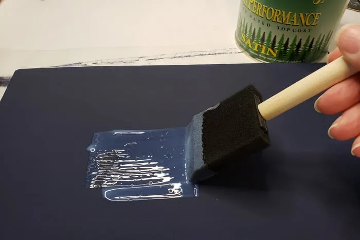 Applying clear coat to blue painted board with foam brush.