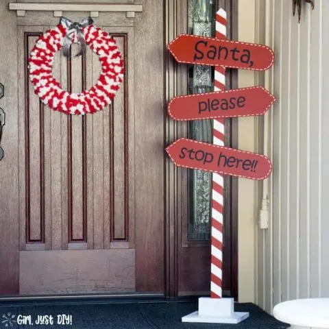 Red and white christmas wreath on porch with santa stop here sign.