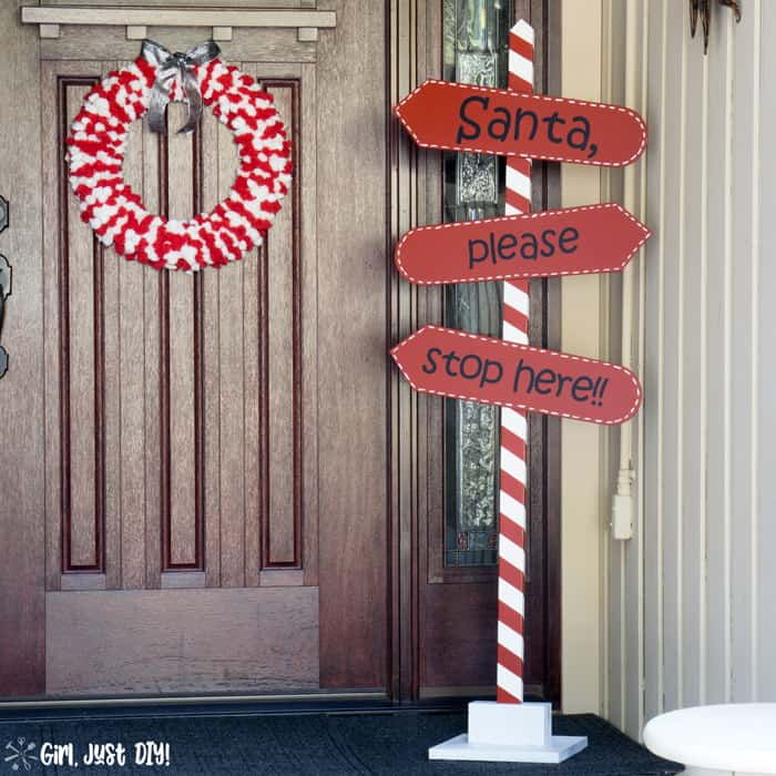 Red and white christmas wreath on porch with santa stop here sign.