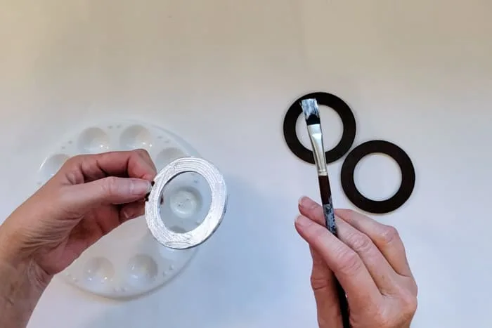 Painting a wood circle with pearl metallic paint with 2 in the background.