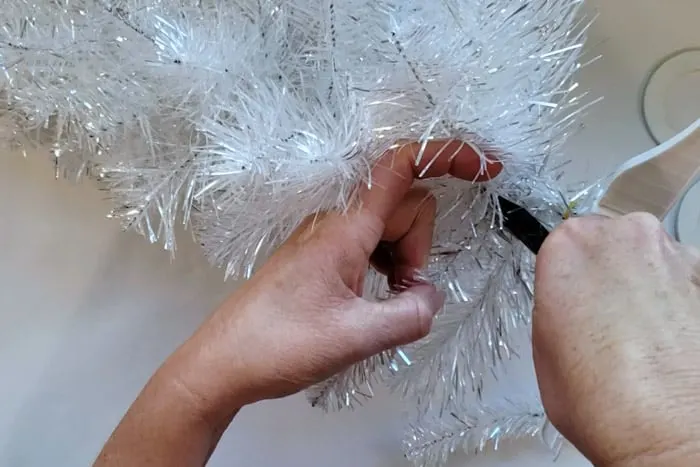Using wire cutters to cut a branch from a silver metallic Christmas Tree.