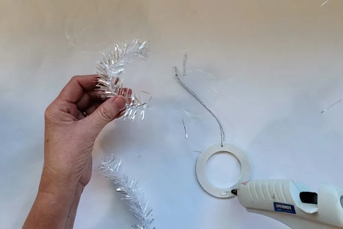 Curved tinsel branch getting hot glued to painted wood circle.