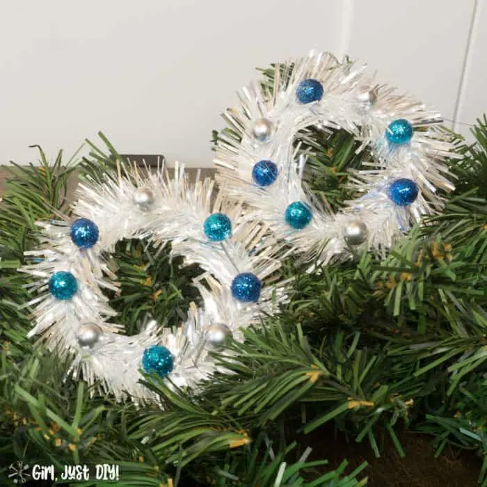 Side by side tinsel mini wreath ornaments on green tree.