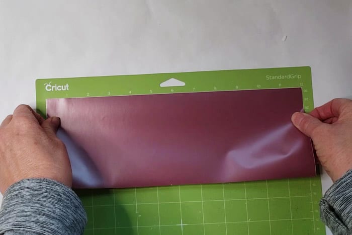 Rose gold vinyl being placed on green cricut sticky mat.