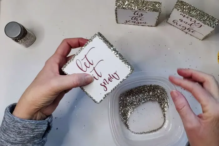 Dipping Christmas Wood Signs into chunky glitter.