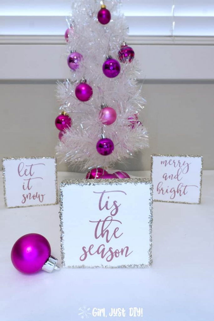 Tis the Season wood sign for Christmas in front of white Christmas tree.