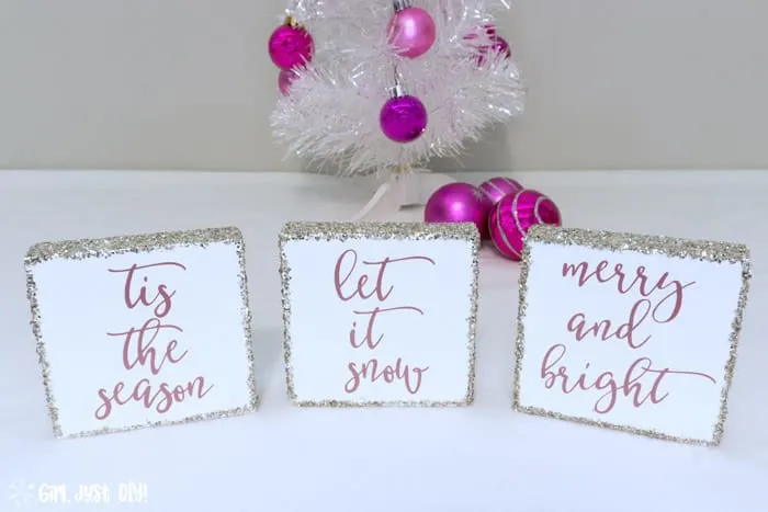 Three Christmas wood signs in front of White Christmas tree with pink ornaments