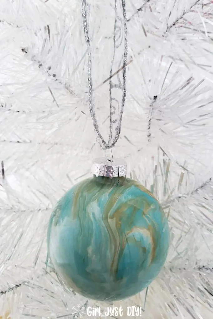 Turquoise and gold ornament hanging against white Christmas tree.