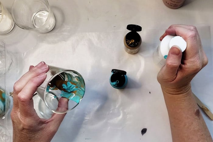 Turquoise, gold and white paint getting layered in a glass votive holder.