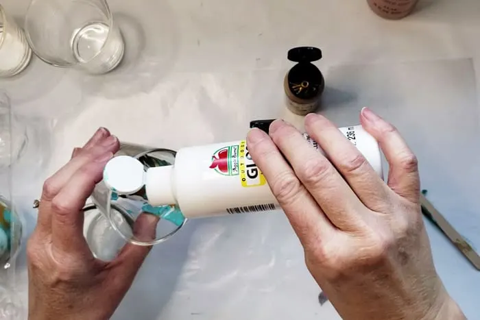 Squirting white craft paint into votive candle holder.