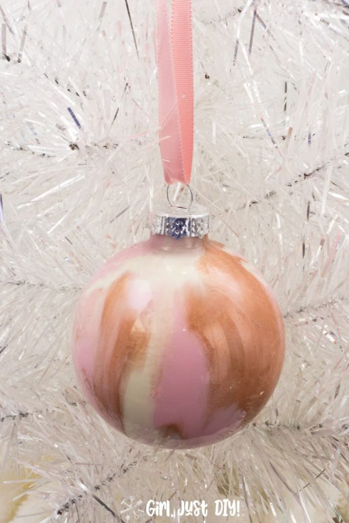 Pink paint pour christmas ornament hanging on white christmas tree.