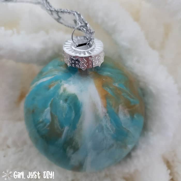 Turquoise, gold and white paint pour Chirstmas ornament on fluffy white yarn.