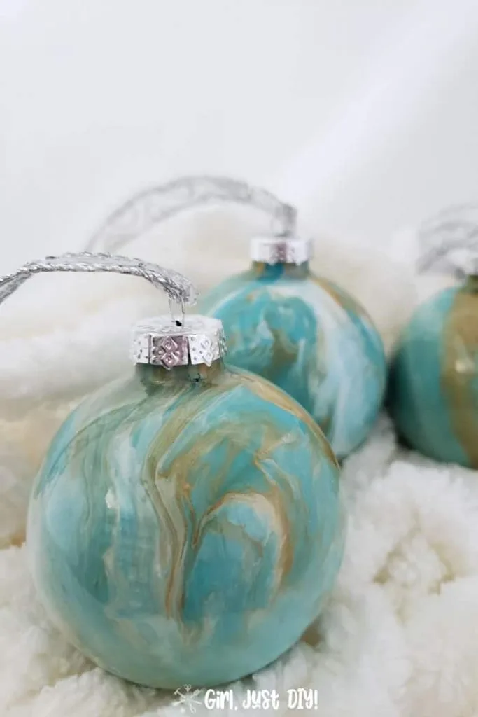 Three paint pour Christmas ornaments on fluffy white yarn.