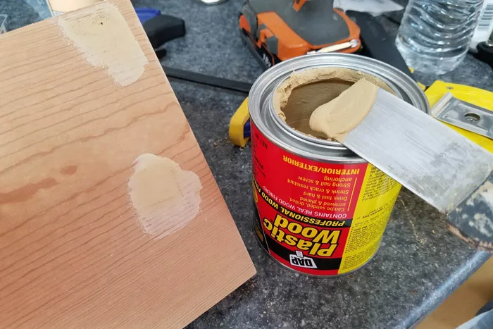 Filling screw holes with putty knife filled with plastic wood filler