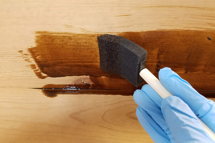 applying dark stain to coat rack with foam paint brush