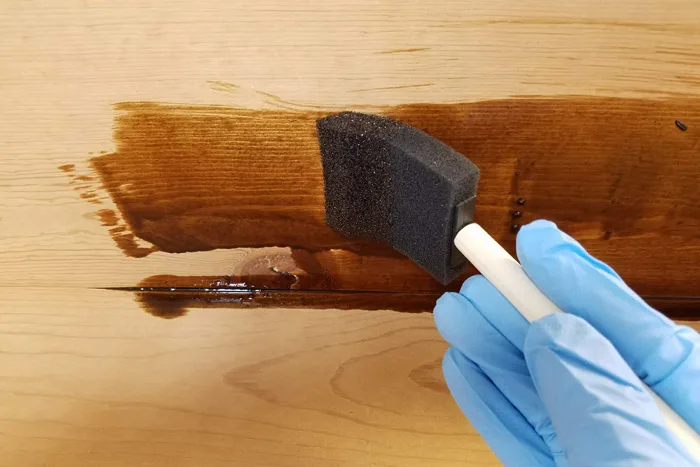 applying dark stain to coat rack with foam paint brush