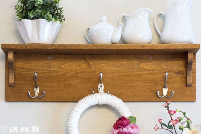 Front image of DIY Wooden coat rack attached to wall with wreath hanging from center hook and white vases on the shelf.