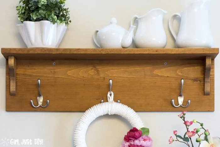 Front image of DIY Wooden coat rack attached to wall with wreath hanging from center hook and white vases on the shelf.