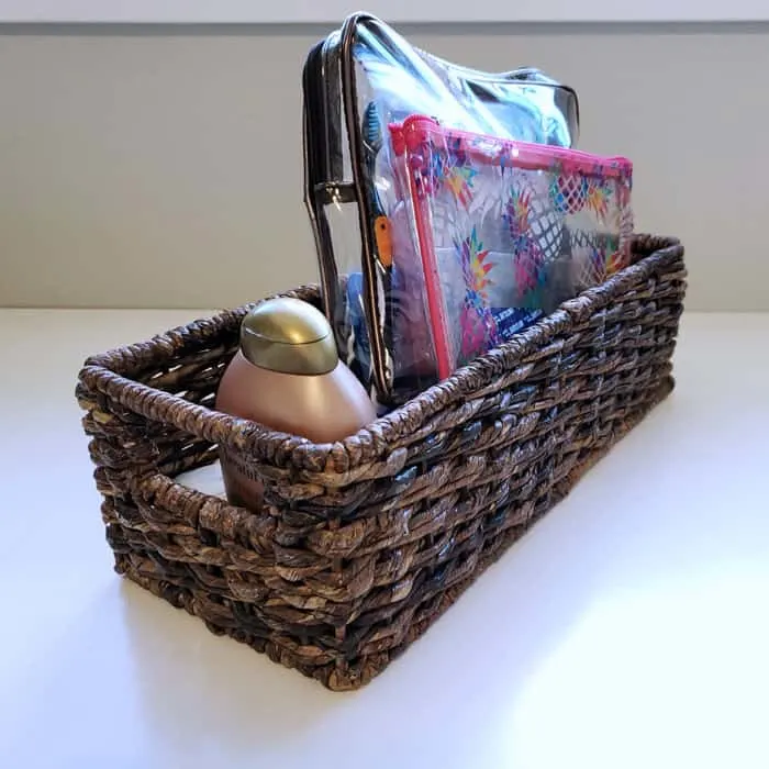 Dark wicker cd basket on white table holding plastic toiletry bags.