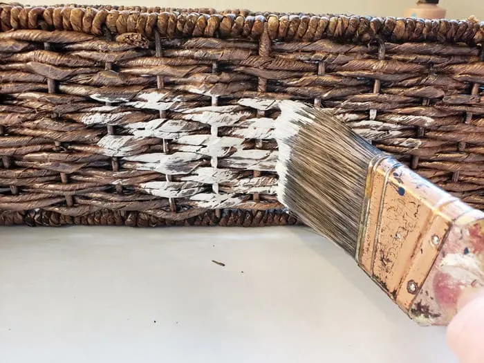 Paint brush whitewashing dark wicker basket.