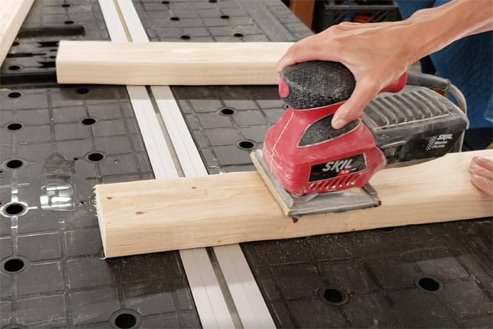 Sanding 2x4s with electric palm sander.