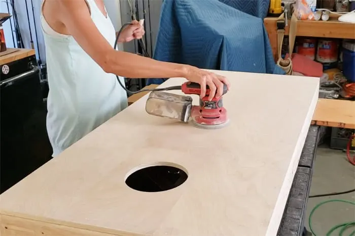 Sanding top of cornhole board with orbital sander.