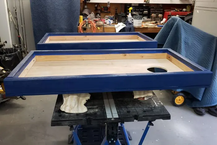 Both cornhole boards painted blue drying on workbench