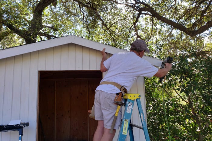 Man on ladder nailing trim to shed face.