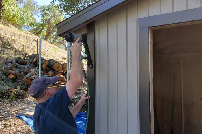 Man nails trim to corner of 8x10 storage shed.