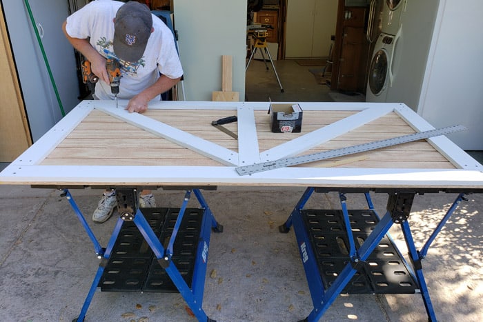 man attaching wood trim to shed door while on saw horses