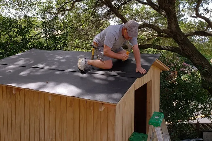 man stapling roofing felt to storage shed roof sheathing.