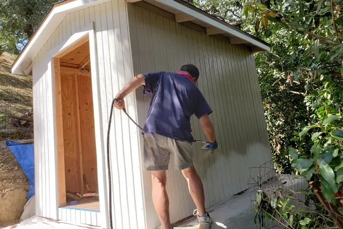 man using airless paint sprayer to paint 8x10 garden shed