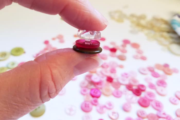 fingers holding two buttons stacked with smaller clear button on top.