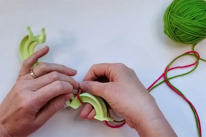 hands wrapping pink yarn around pompom maker