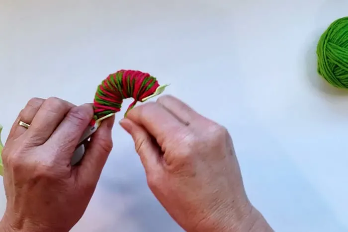 hands wrapping yarn around full pom pom maker