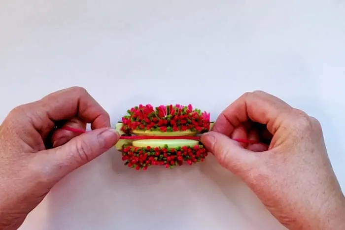 hands tying yarn around both halves of pom pom maker