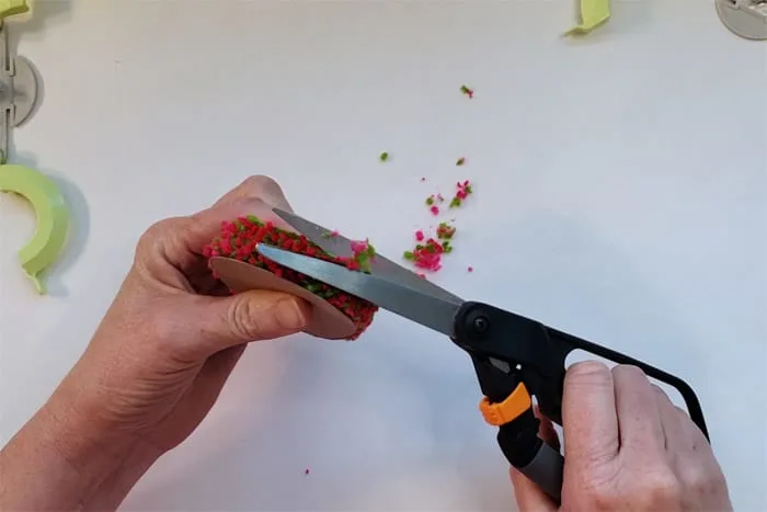 scissors trimming pompom sandwiched between cardboard circles