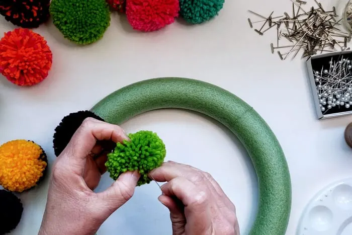 Pinning a green pompom to a wreath form.