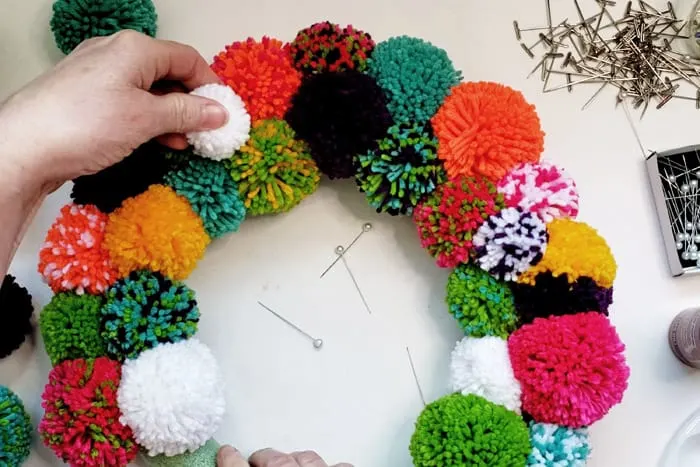 adding small white pompom to colorful diy pompom wreath