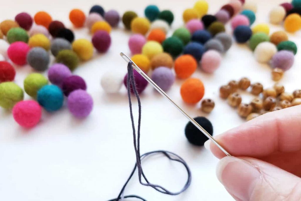 long threaded needle with colroful felt balls in the background