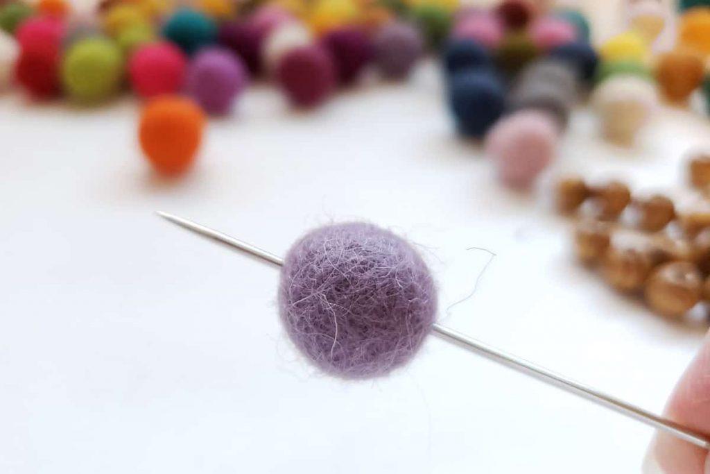 lavendar felt ball threaded onto long needle with colorful felt balls iin background