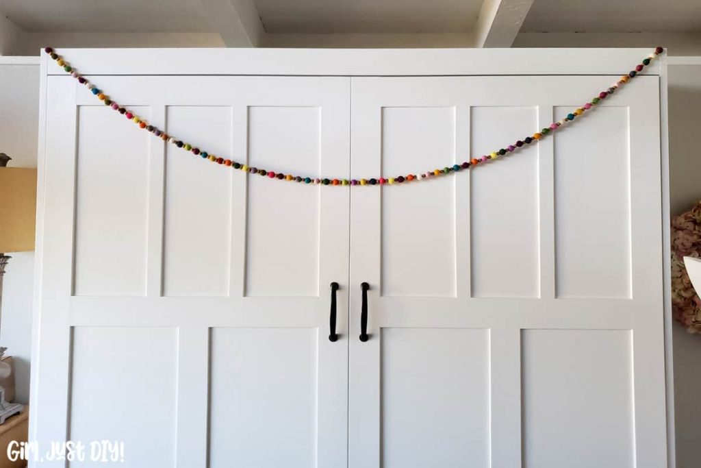 Colorful felt ball garland hanging across white cabinet face.